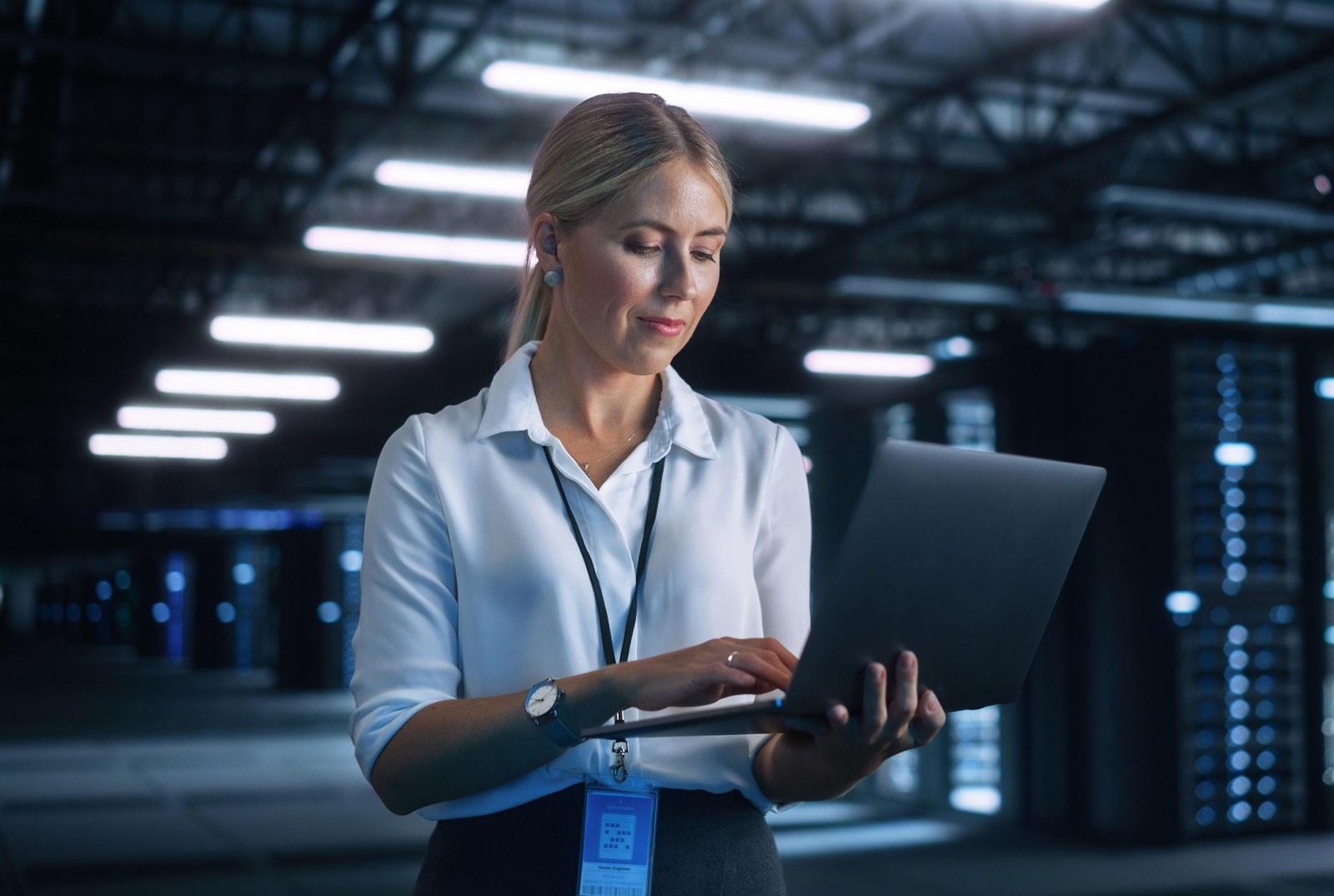 Ingénieure cloud avec un ordinateur portable dans une allée de datacenter